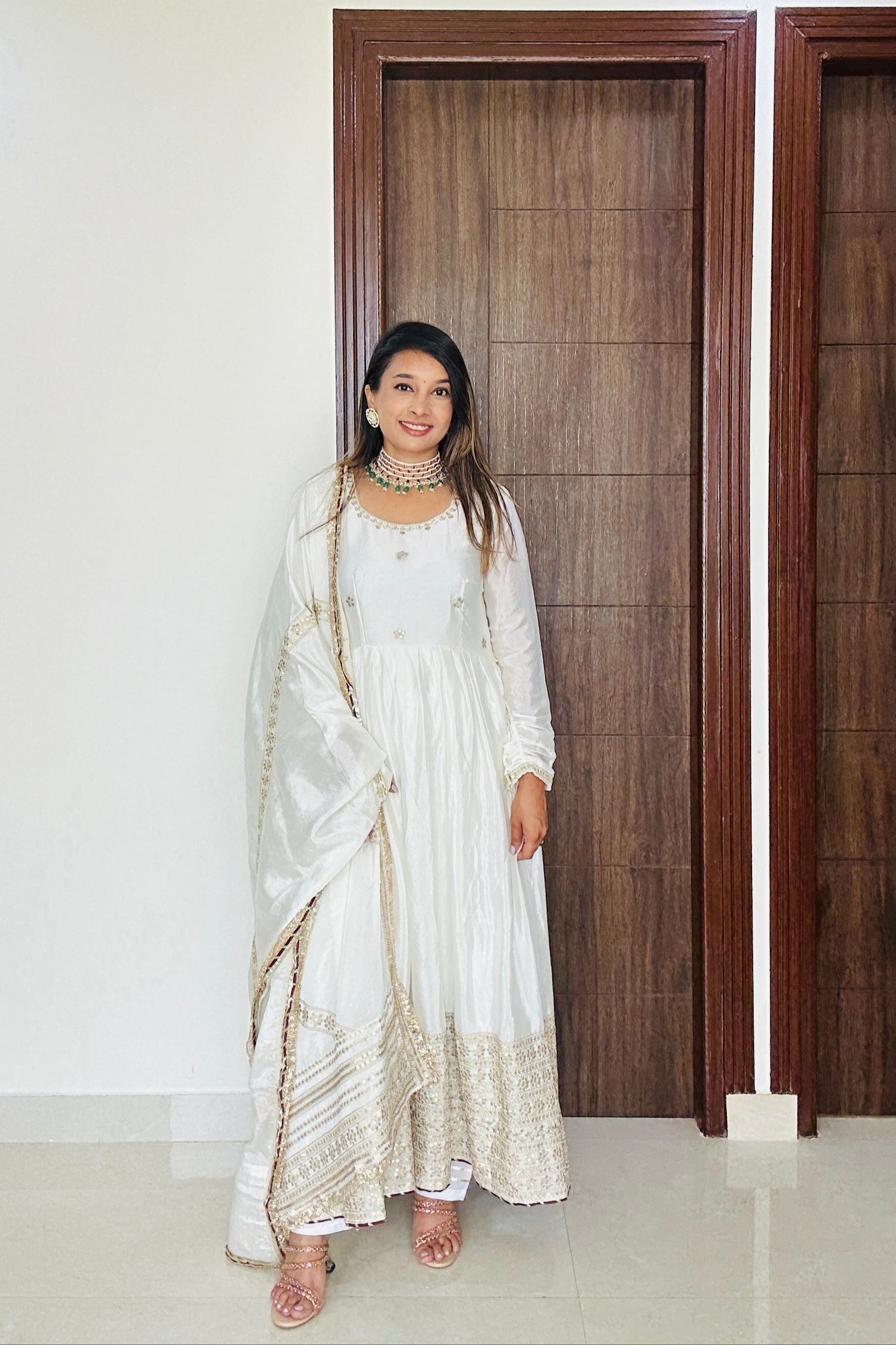 Woman in a white traditional outfit standing in a room with wooden doors.